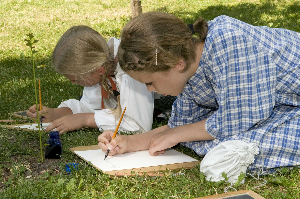 Ferieskolen uke 27, 2009.
Undervisning foregår utendørs, barna lærer å skrive med blekk.
