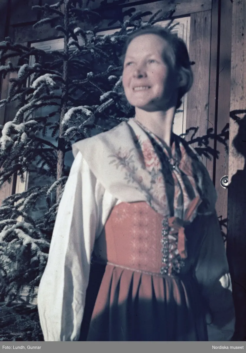 Dalarna. På Långbergsgården i Tällberg på vintern med kvinna i folkdräkt och bakom henne en gran.