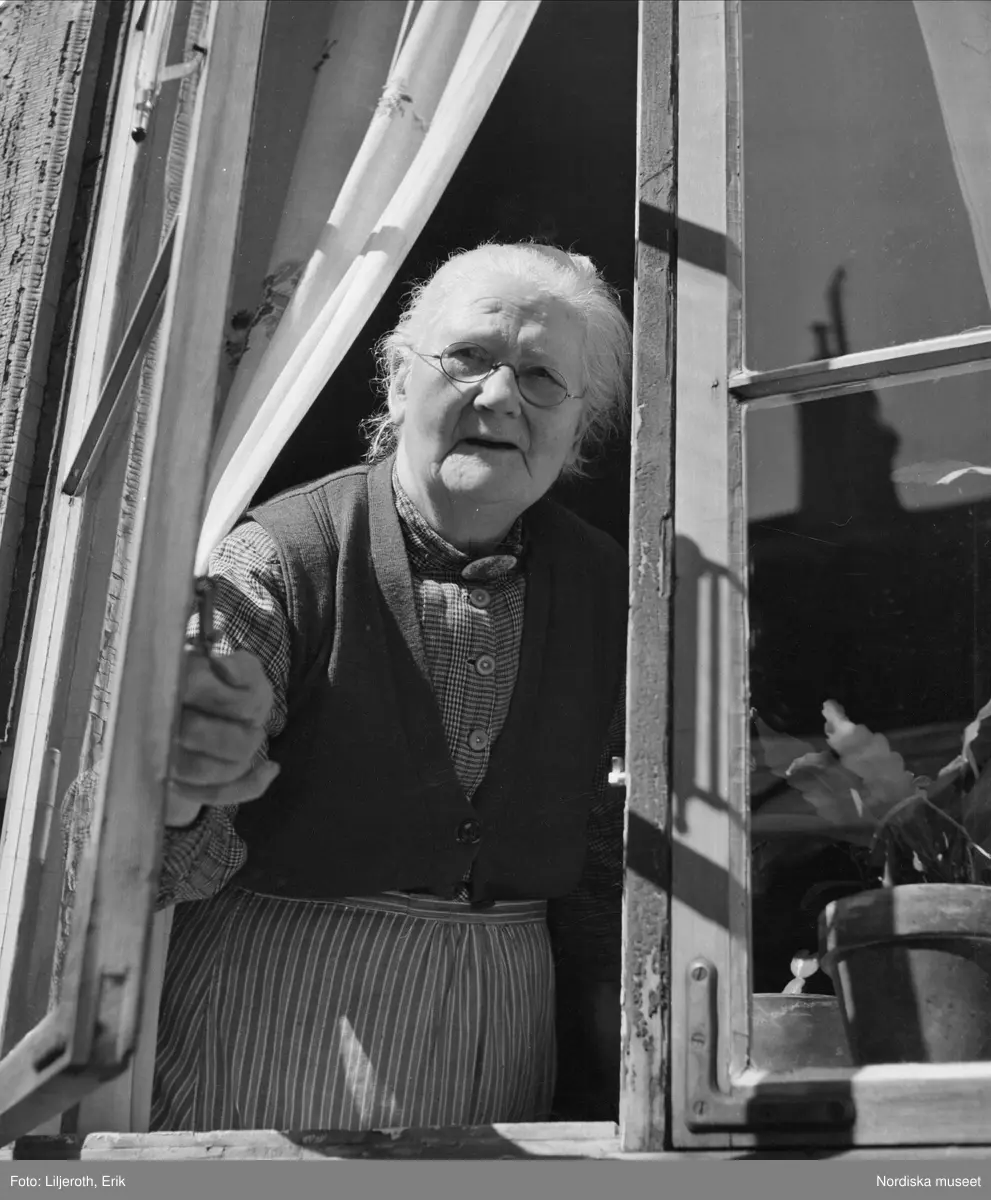 Göteborg. En äldre kvinna som tittar ut genom ett öppet fönster