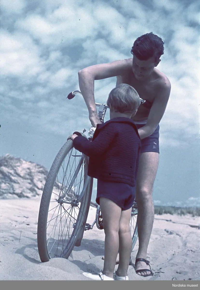Man med cykel och en liten flicka på en sandstrand.