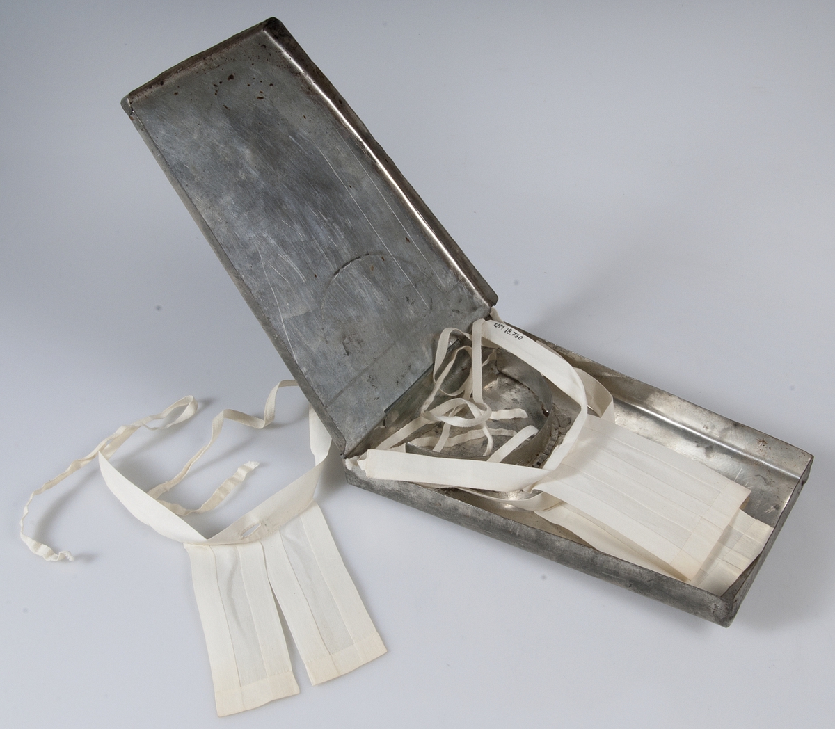 Tre st prästkragar, s.k. elvor, i vitt stärkt linne med knytband. Tillhörande förvaringsask av plåt se UM18730b.