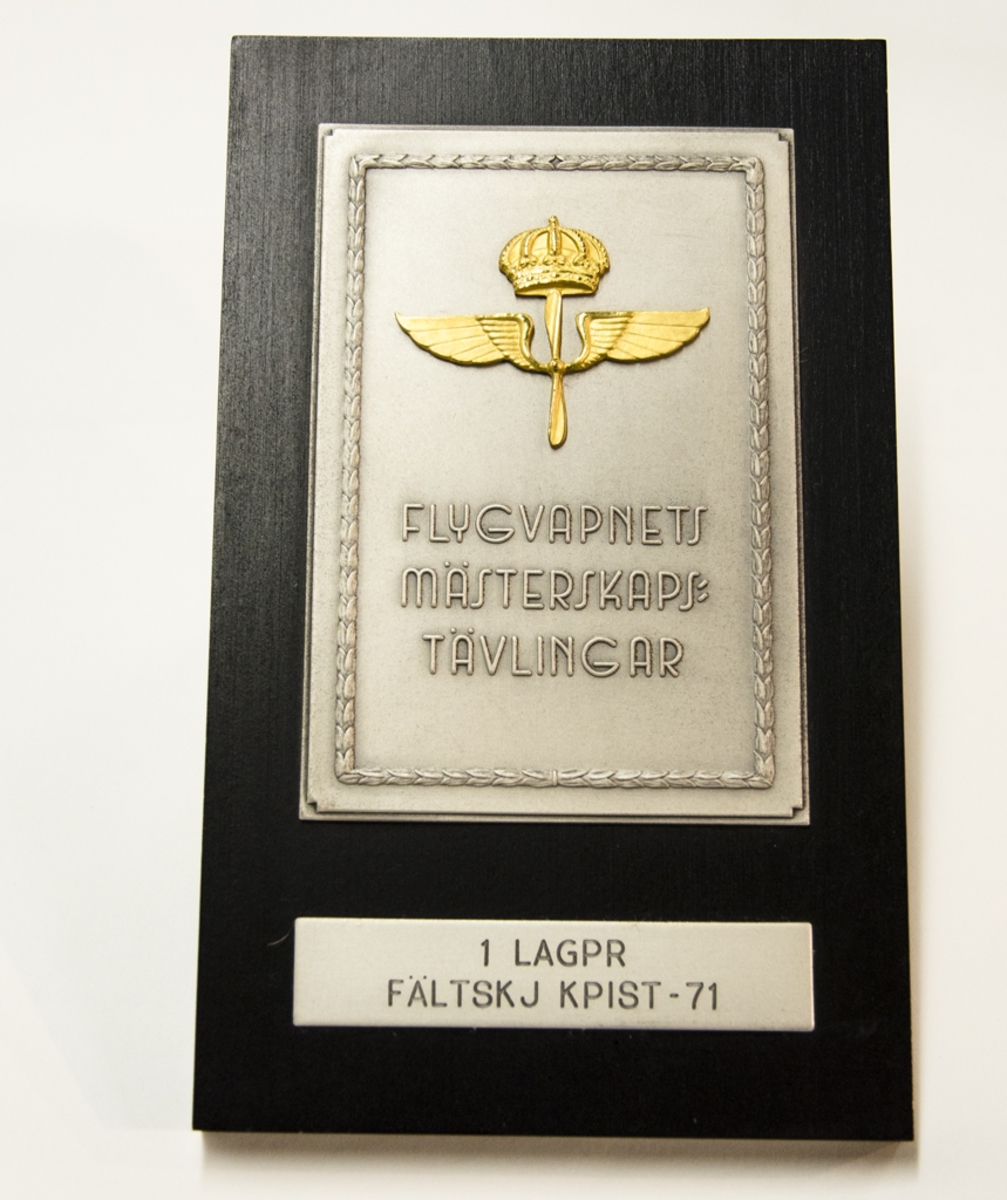 Plakett med flygvapnets krönta emblem samt texten: "FLYGVAPNETS MÄSTERSKAPSTÄVLINGAR 1:A LAGPRIS FÄLTSKJ. KPIST - 71".