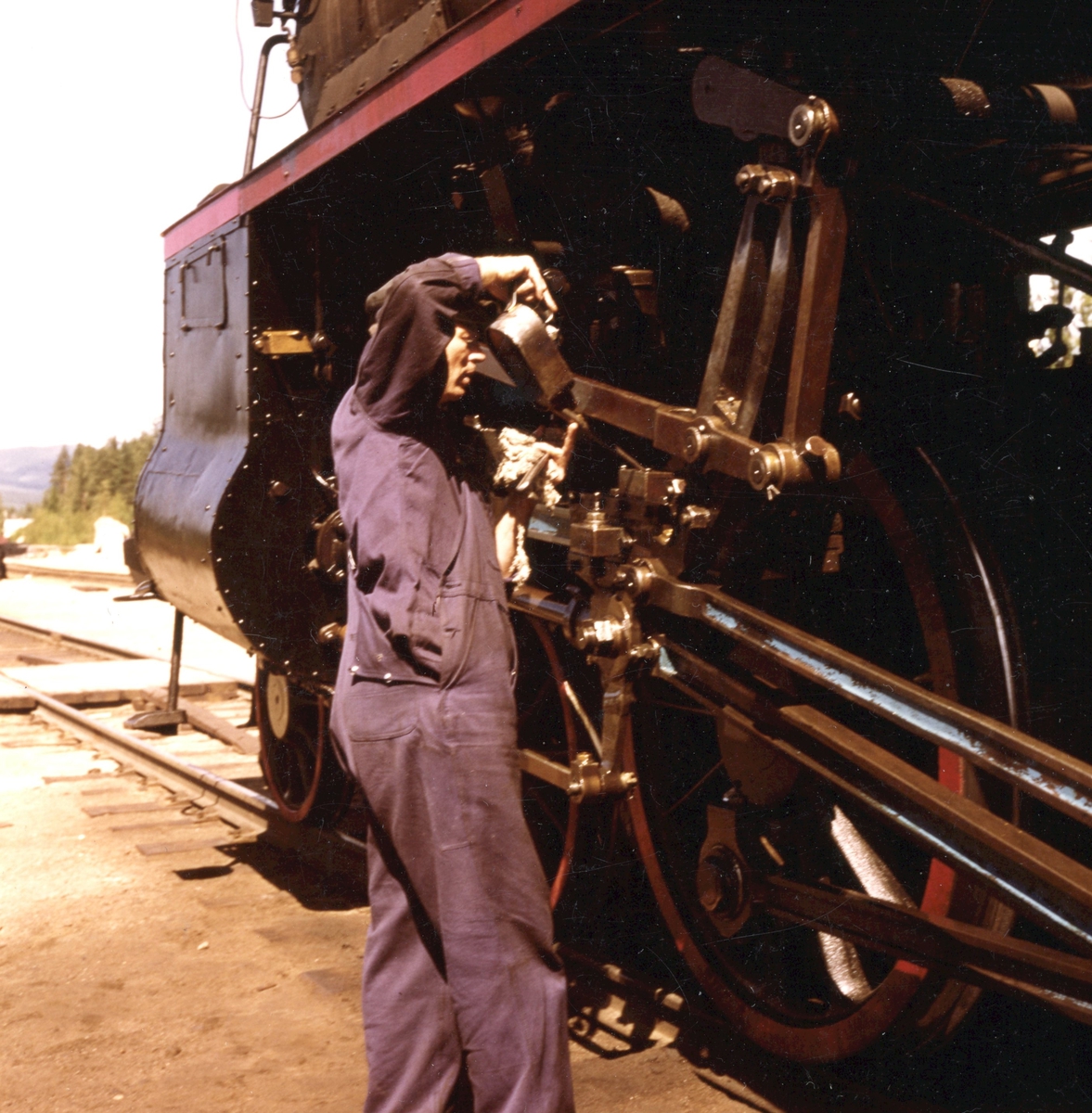 Fyrbøteren smører gangtøyet på damplokomotiv type 26c nr. 414 under oppholdet på Koppang stasjon