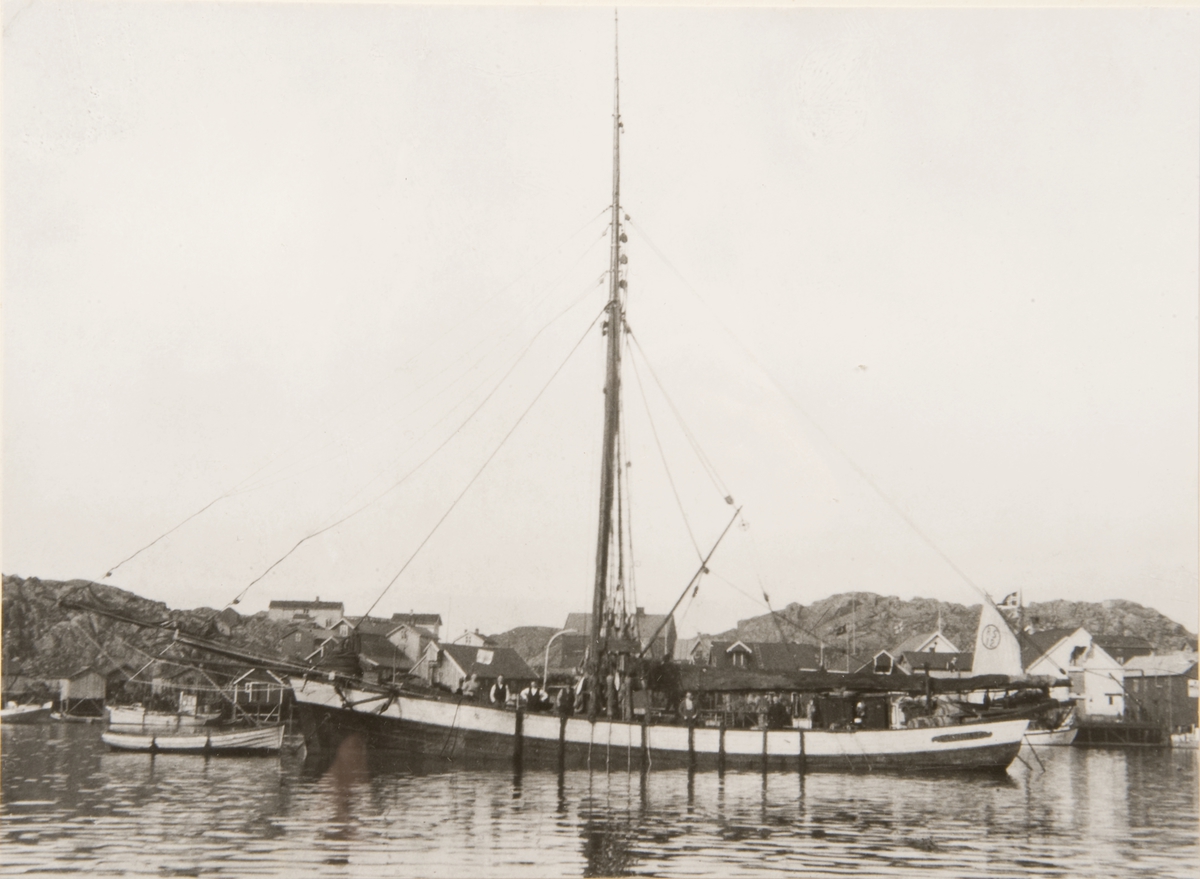Jakt 'Mathilde' (b. 1884, Ølve, Hardanger) i havnemiljø med sjøhus og RS 12 i bakgrunnen