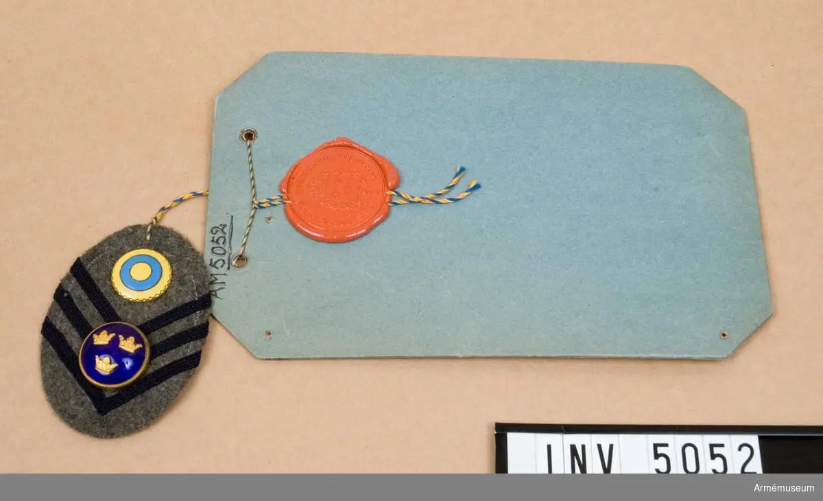 För officer.Modell å ovanstående fastställd 11 maj 1943.Ett elipsformat märke av kommisskläde med i detta fall tre vinklar av mörkblått silkeband. Har knapp för officer m/1865 och neutralitetsmärke i blå och gul emalj. 