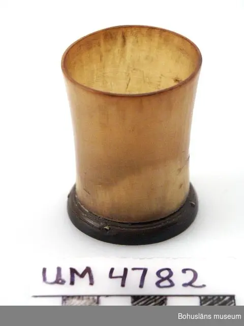 Ur handskrivna katalogen 1957-1958:
Supglas av horn
H. 5,5; mynn. D. 4,2; fotens D. 4,2 cm; bottenplattan, av mörkare horn, är nitad fast. Helt.

Lappkatalog: 65

Bottenplattan, av mörkare horn, är fastnitad med fyra "mässingpliggar".