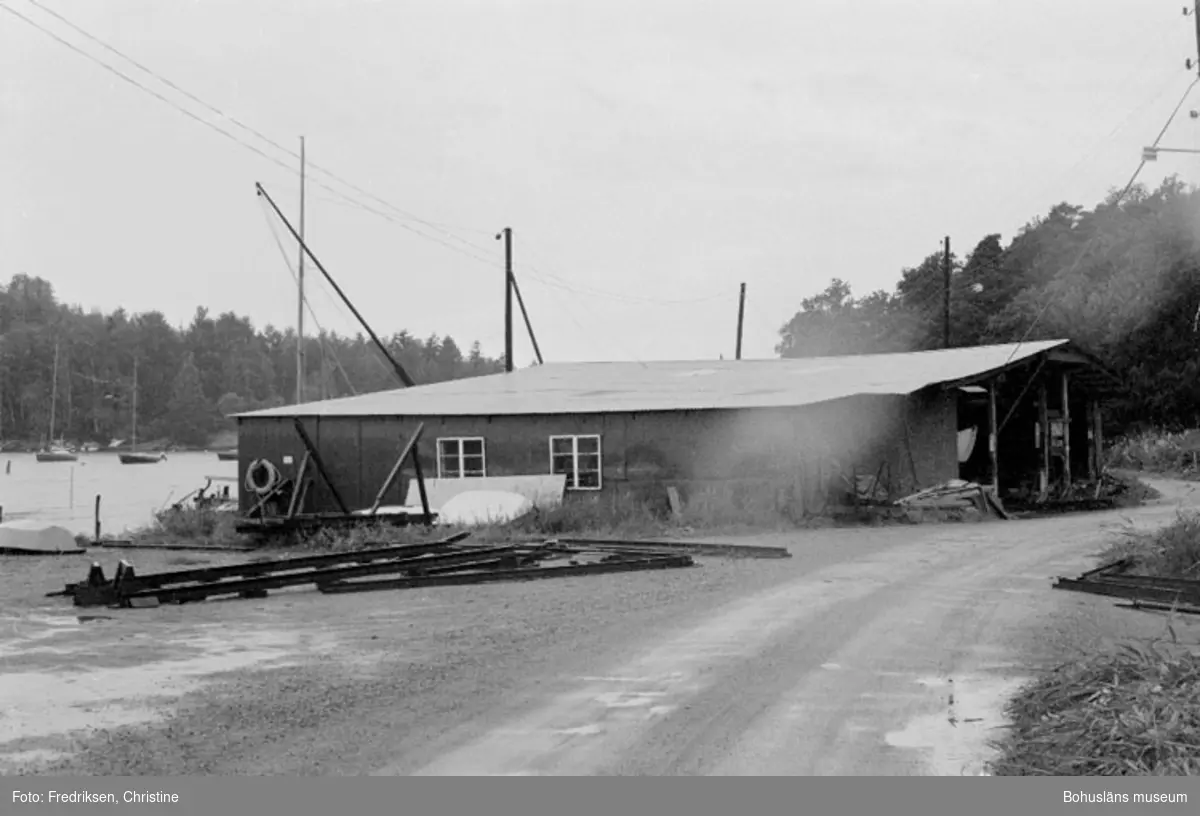 Motivbeskrivning: "Evert Wikströms varv i Ulvesund. På bilden syns verkstad uppförd 1950 (senare ombyggd), på vänster hand plan för vinterförvaring av båtar."
Datum: 19800716
Riktning: Sv