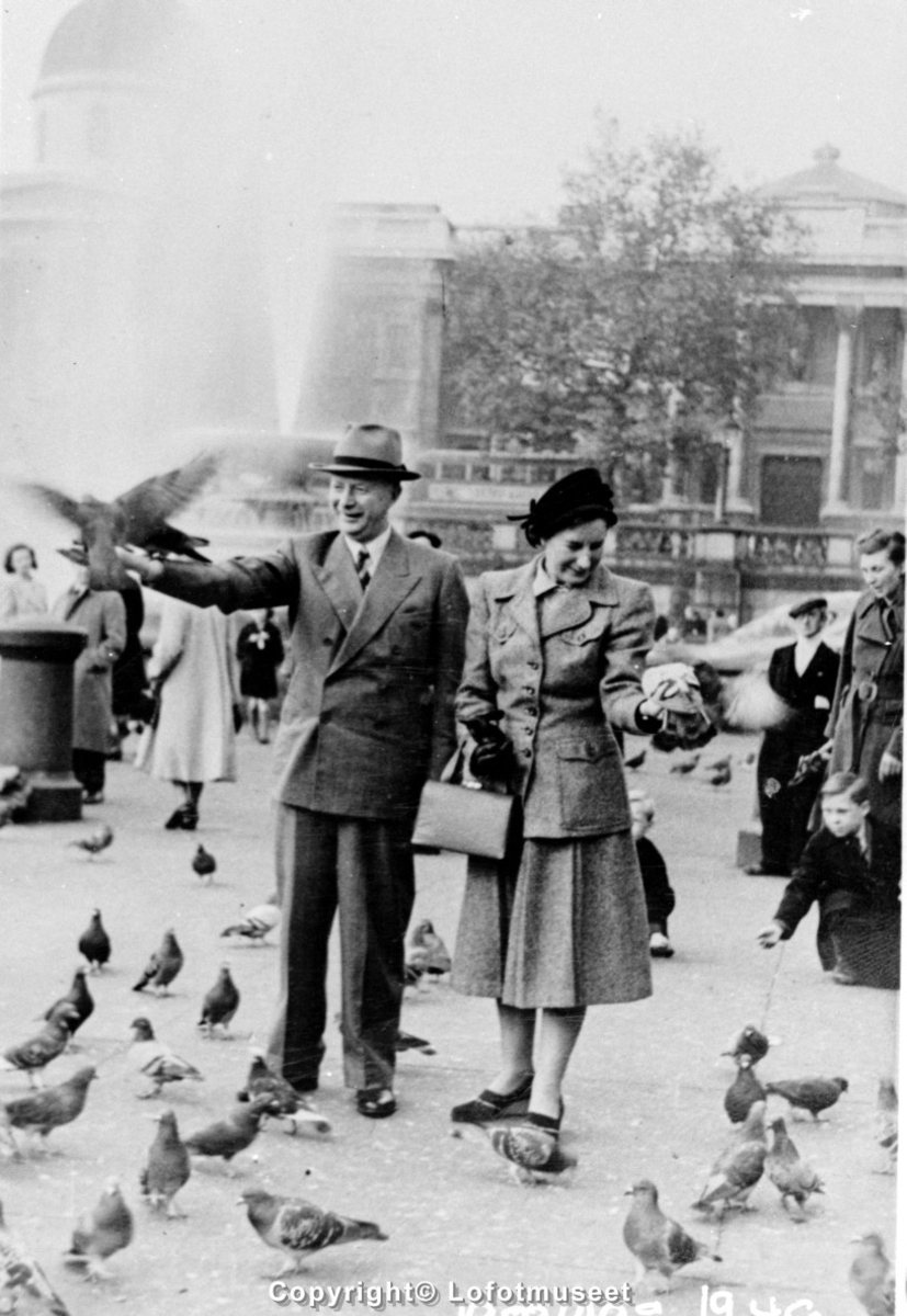 Man og kvinne mater fugler på et torg i en storby i utlandet. 1940-1950 tall