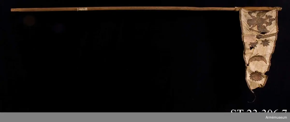 Duk av vit sidentaft och strumpa av rött linne försedd med frans vid öppningarna. Motivet målat i guld- och silver samt rött och grönt bestående av en krönt örn, måne, sol och stjärnor, På duken en pappersetikett som anger att den tagits i slaget vid Saladen 1703.
