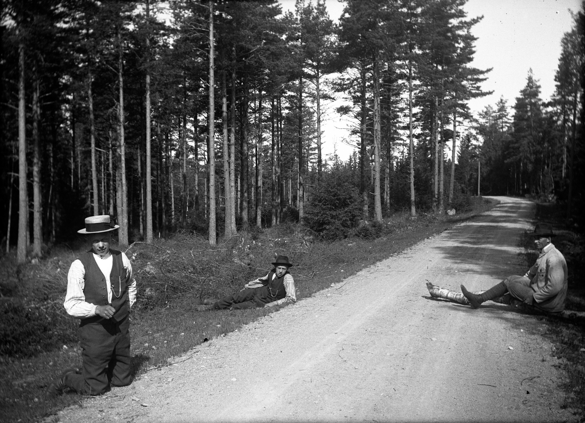 Tre män tar en paus vid vägkanten i skogen.