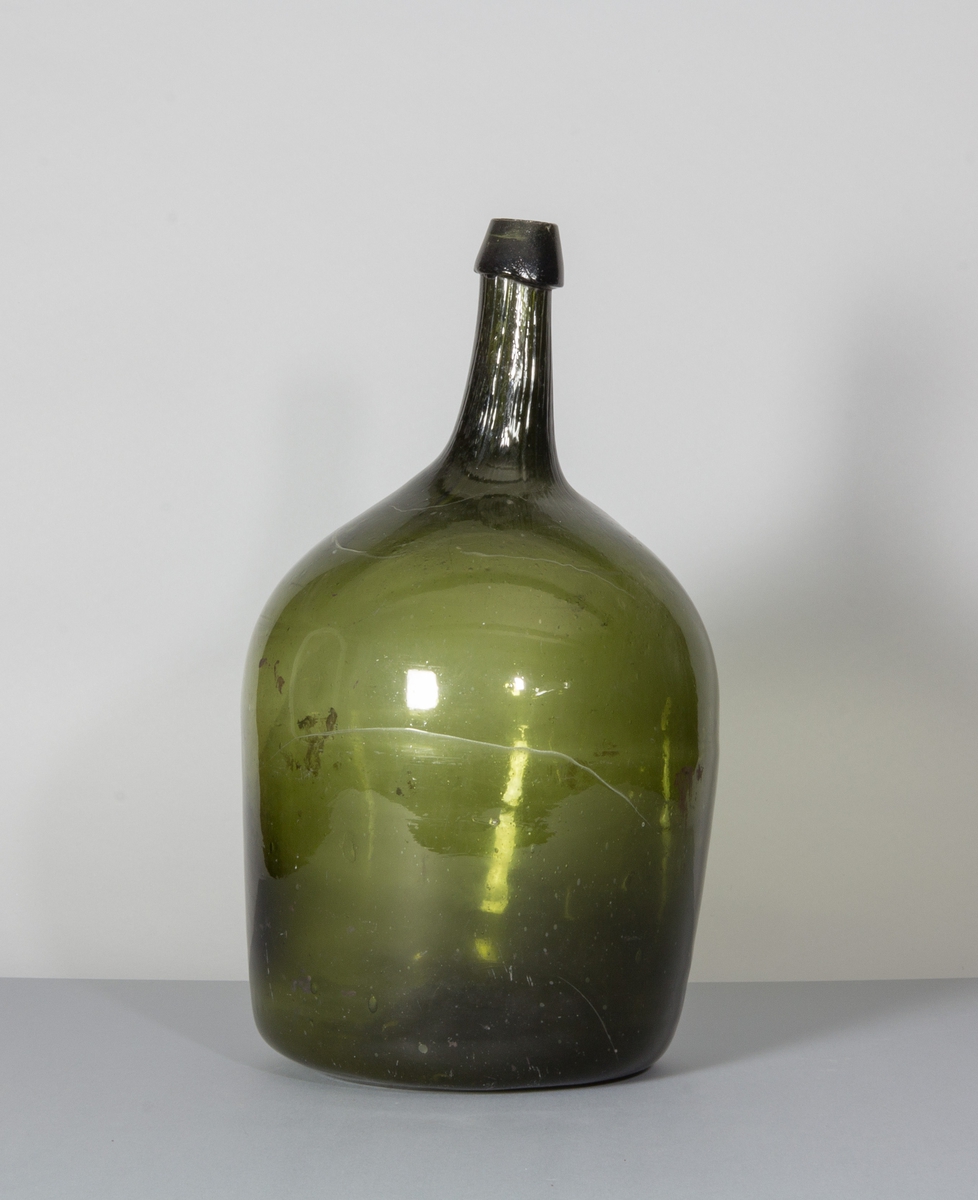 Flaska i grönt glas. Rundade sidor, hals med halsring, flat botten.
Eventuellt använd för förvaring av ättika.