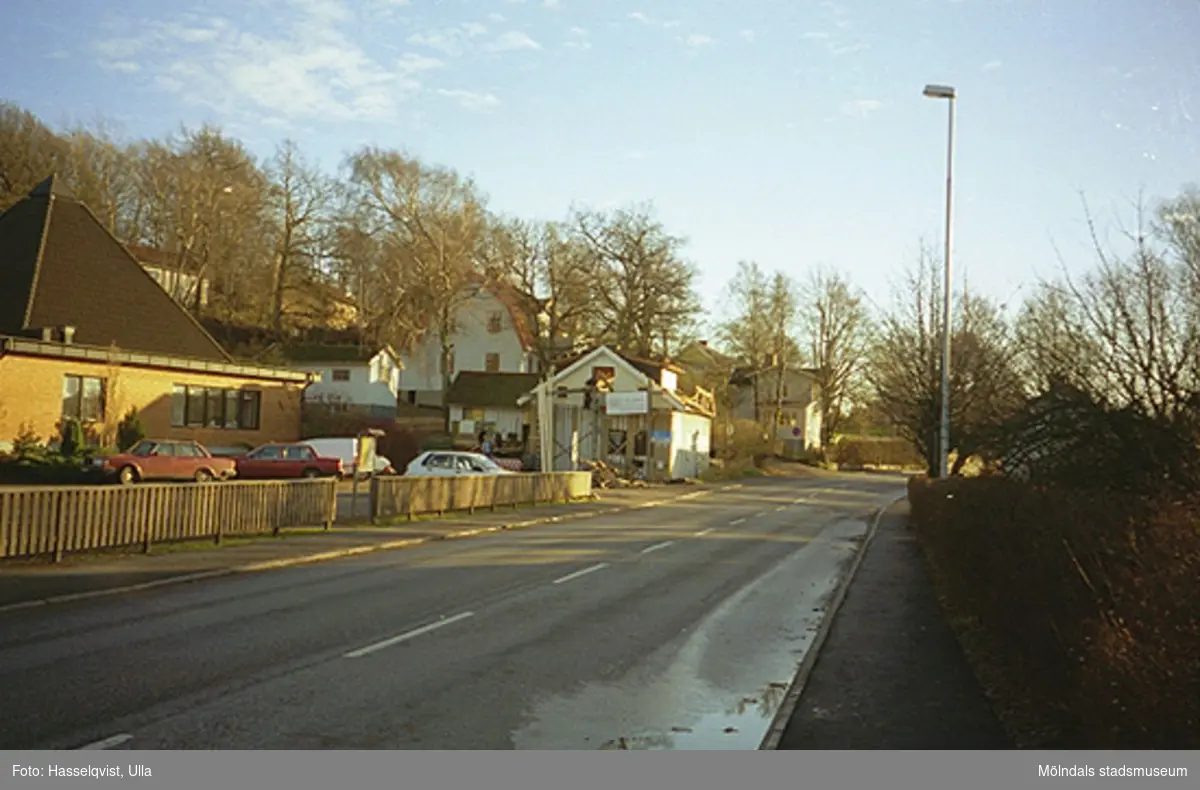 Hantverksgården Ekebacken, december 1994. Det vita trähuset utefter vägen ligger på Gamla Riksvägen 81C i Kållered. Längst till vänster ses Centrumkyrkans parkering.