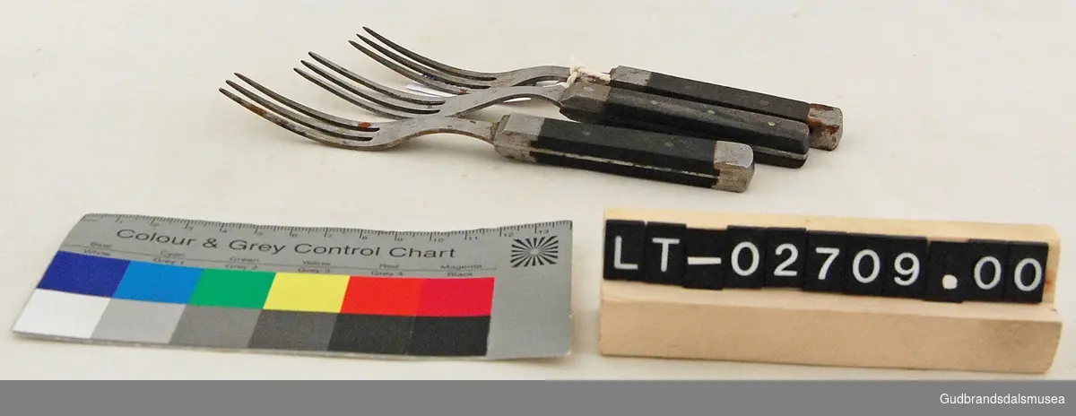 Tre gafler med håndtak i metall og tre som er naglet fast og felt inn i metallet på midten av håndtaket. Nærmest like langt skaft som selve gaffelhodet. 