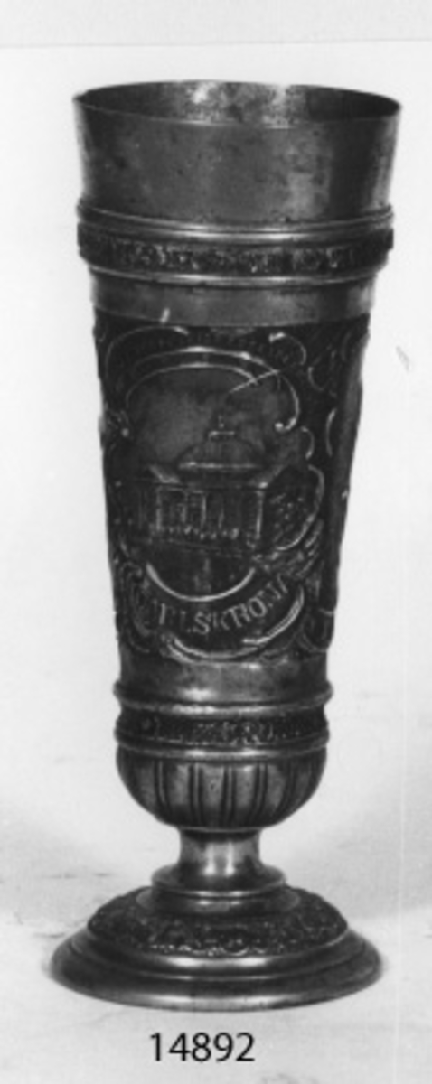 Vas i tenn. Runt vasen i relief följande motiv från Karlskrona: H.M. pansarbåten Oden, klockstapeln, Trefaldighetskyrkan och Carl XI-statyn.