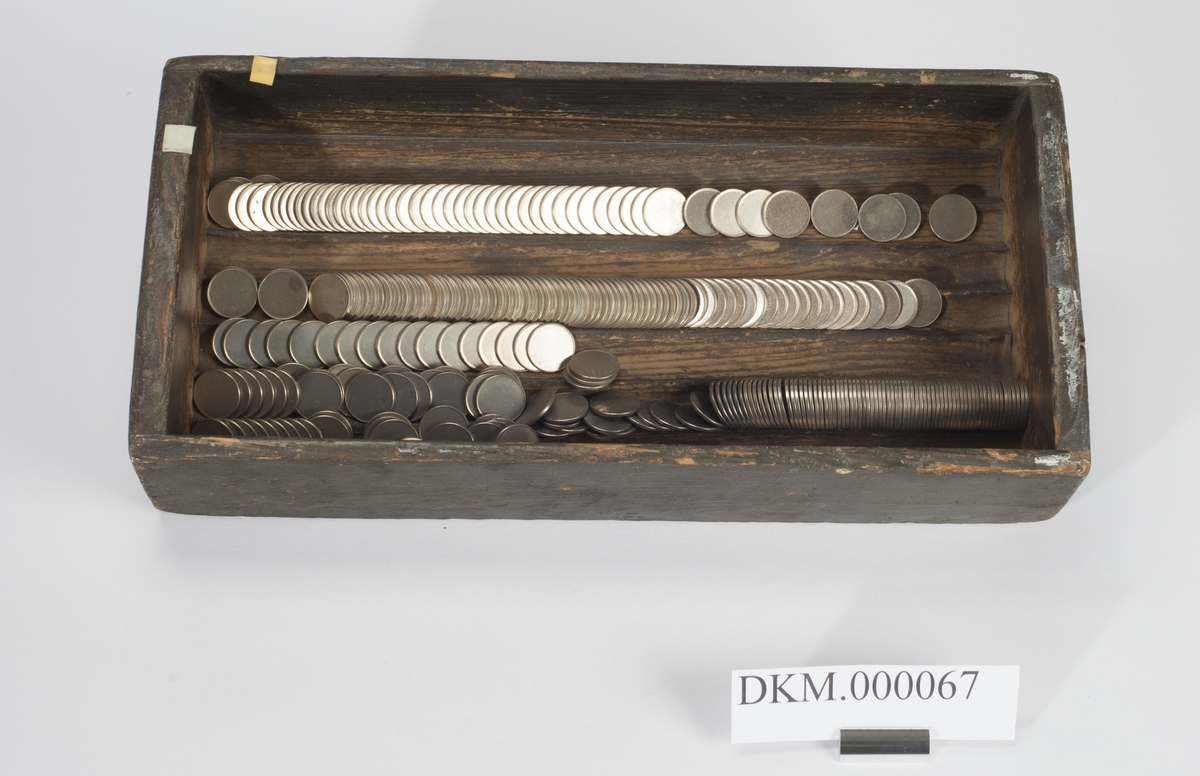 Rektangulær, åpen kasse med langsgående riller til plassering av mynt i bunnen.