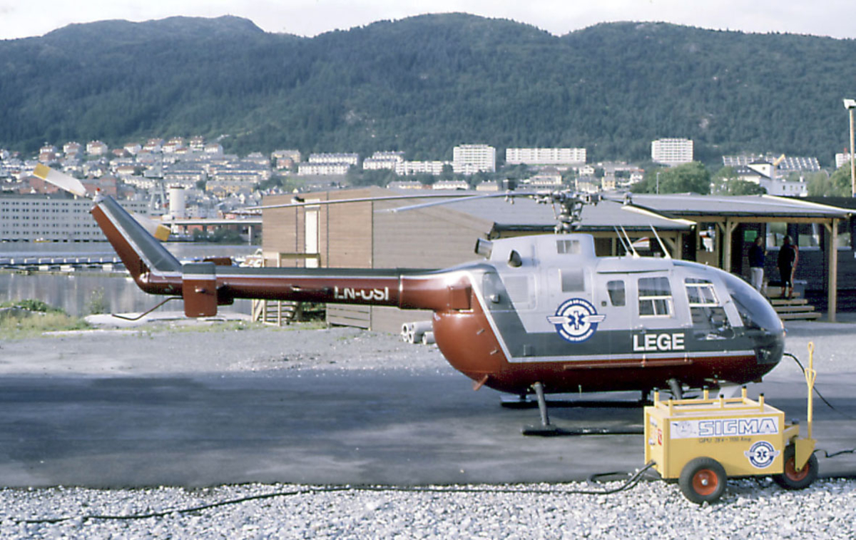 Lufthavn, ett ambulansehelikopter på bakken,  Eurocopter Deutschland HmbH BO 105S, LN-OSI fra Norsk Luftambulanse A/S. Bebyggelse i bakgrunnen