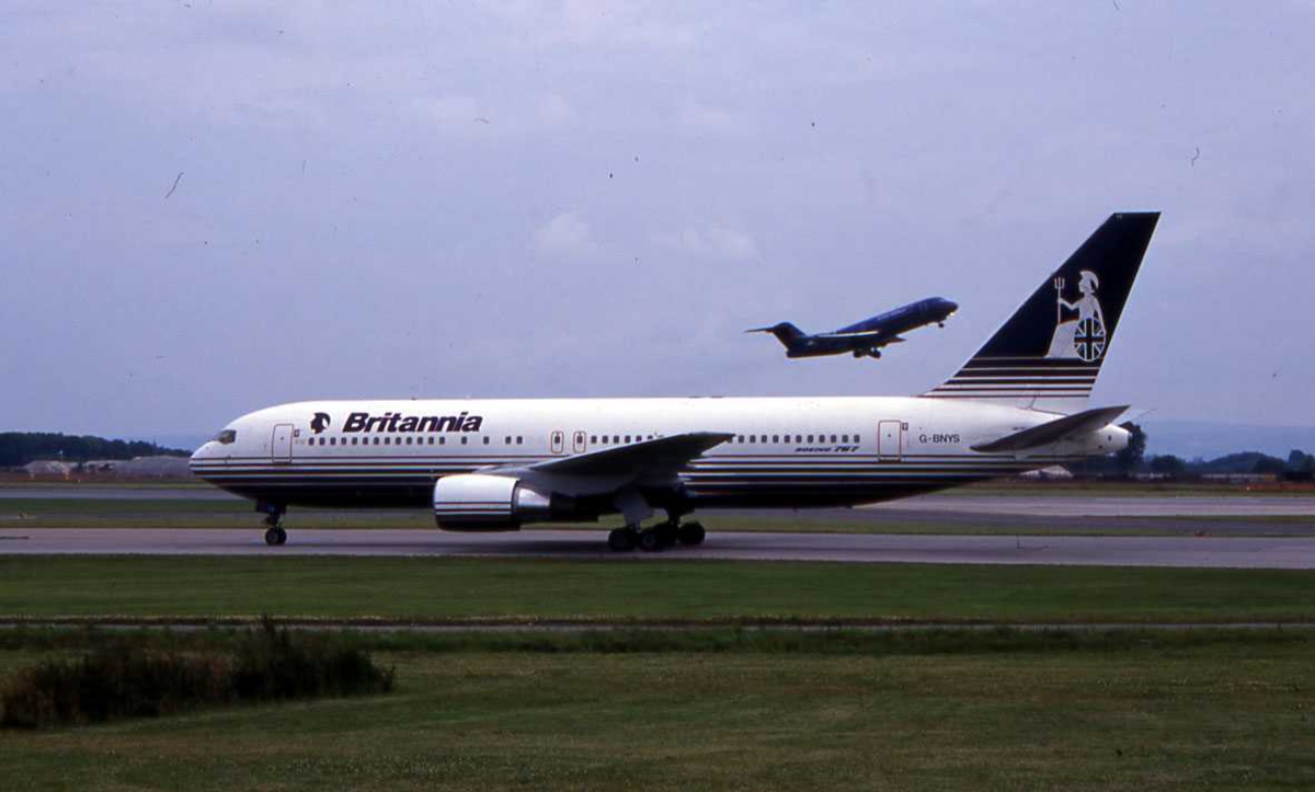 Ett fly på bakken, Boeing 767-204(ER) .G-BNYS fra Britannia. Ett fly tar av i bakgrunn. 