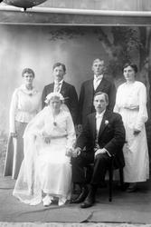 Studioportrett i helfigur av et brudepar med følge.