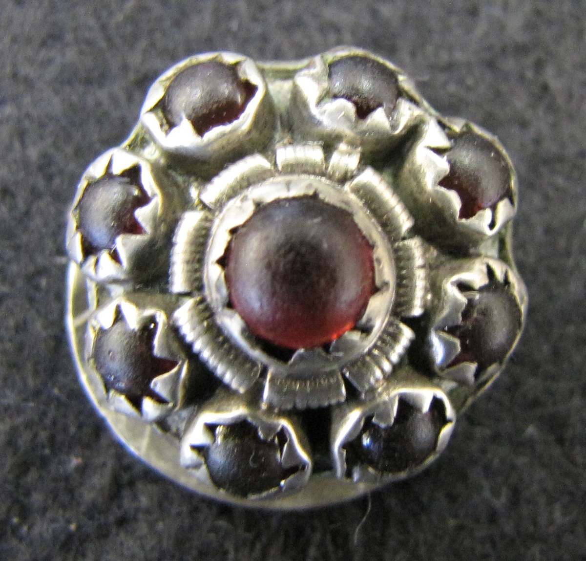 Allmogeknapp av silver, manschettknappsmodell, med nio infattade röda glaspärlor.