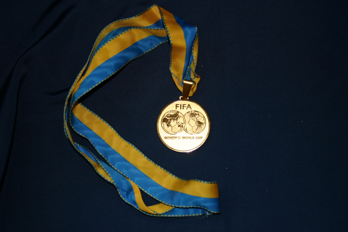 Fra FIFA Women's World Cup i Sverige 1995. Minnemedalje m. blått og gult bånd.