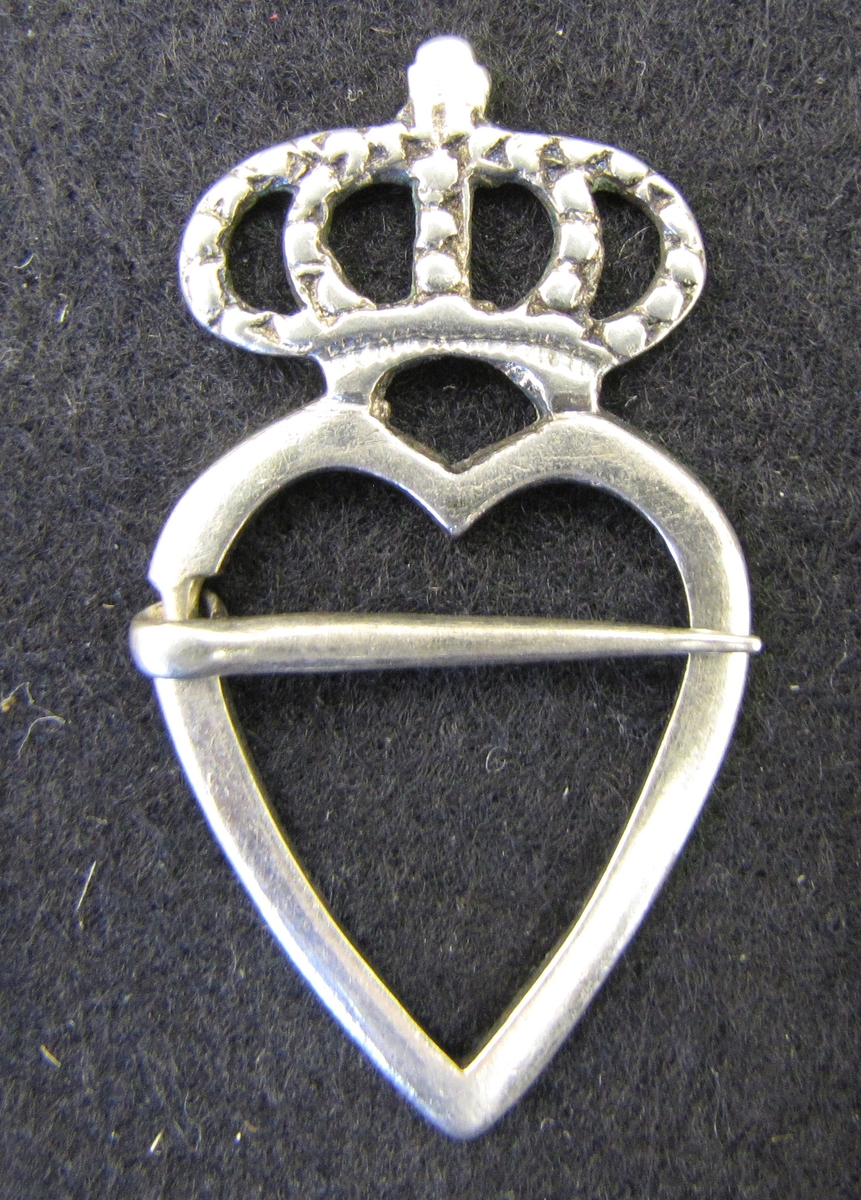 Spänne av silver i form av ett hjärta krönt av en bygelkrona.