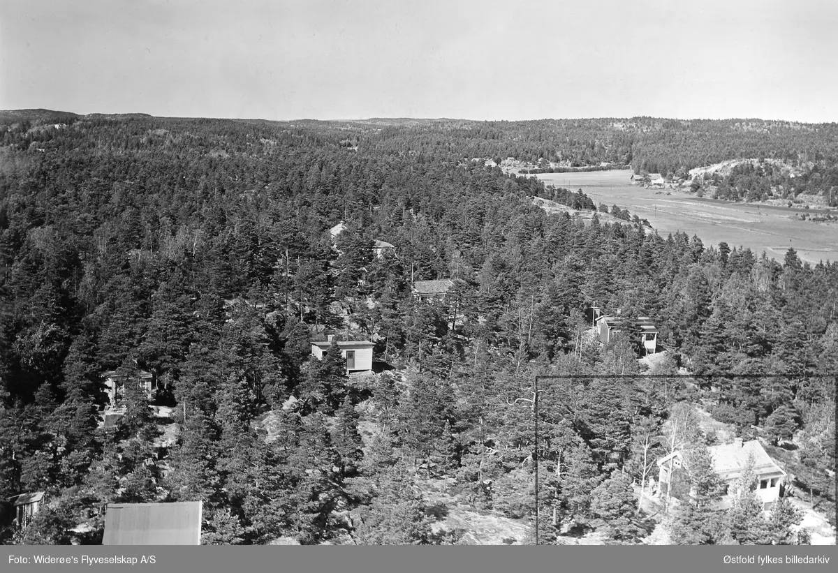 Skråfoto av hytter og gårdsbruk. Holmen i Torsnes, Borge. Flyfoto 19. juni 1959.