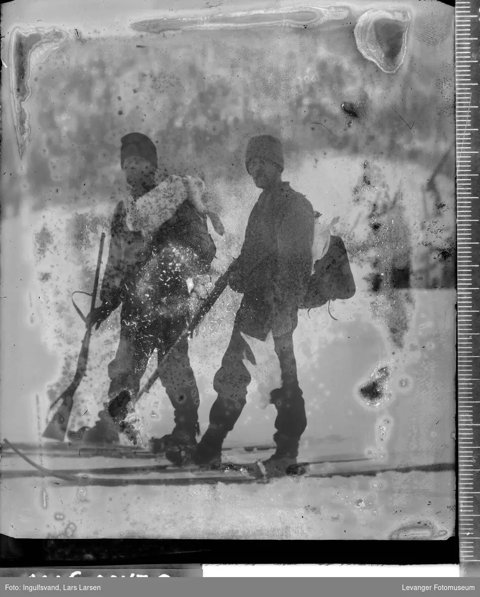 Portrett av to på ski som er på jakt, med geværer, skutt hare og rype.