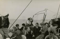 Mange unge kvinner og menn på et båtdekk.