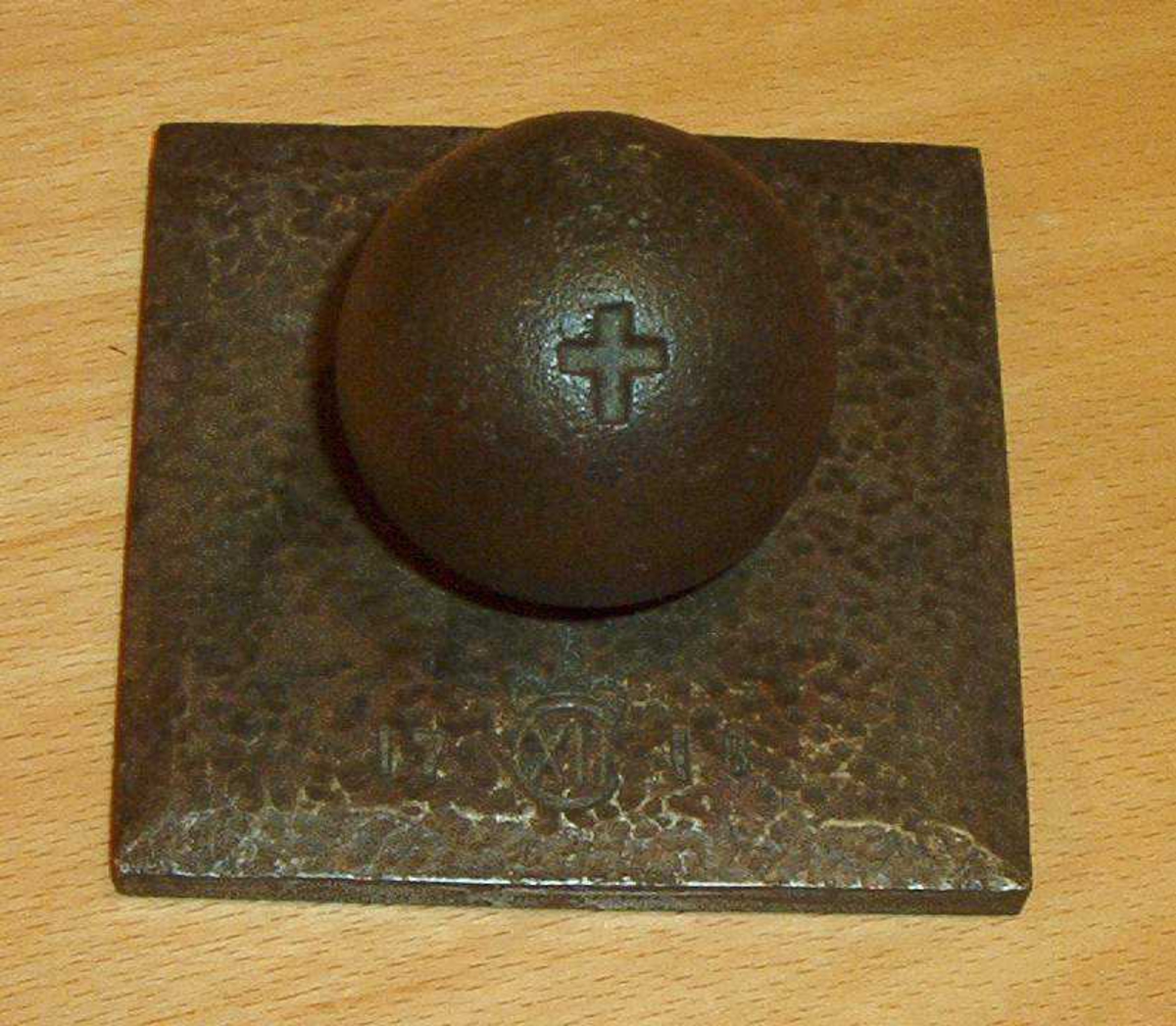 Jernkule skrudd fast i en kvadratisk jernplate.  Et kors er gravert på kulen.  På platen er årstallet 1718 og et monogram.

