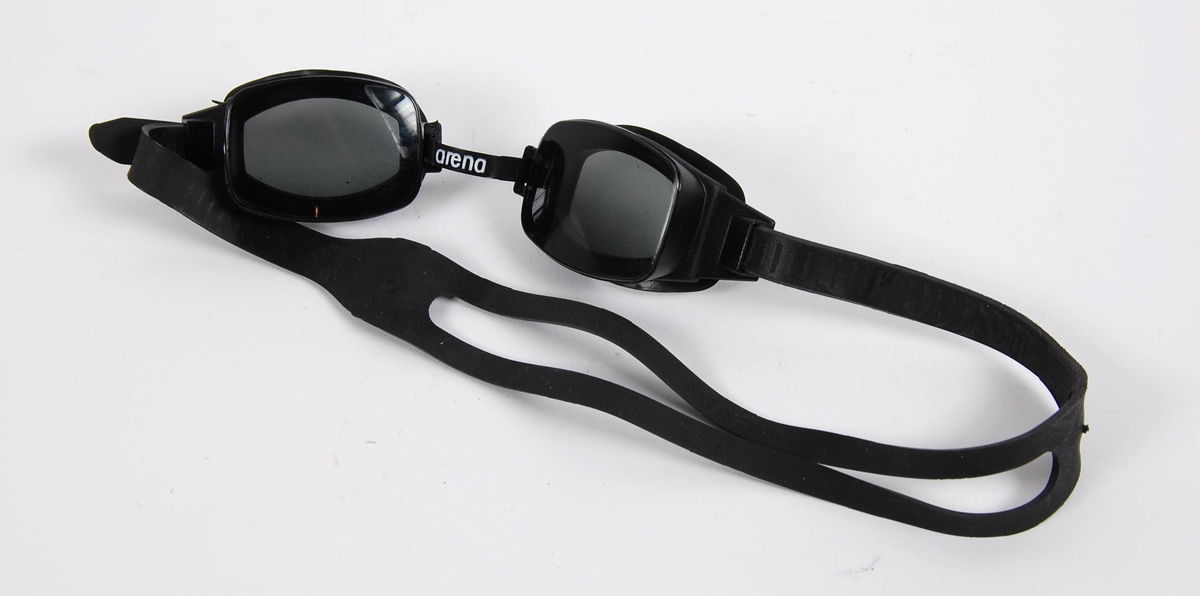 Sort svømmebrille til sort vettedrakt. Brillen har innfatning og glass av plast. Hodereimen er av gummi.