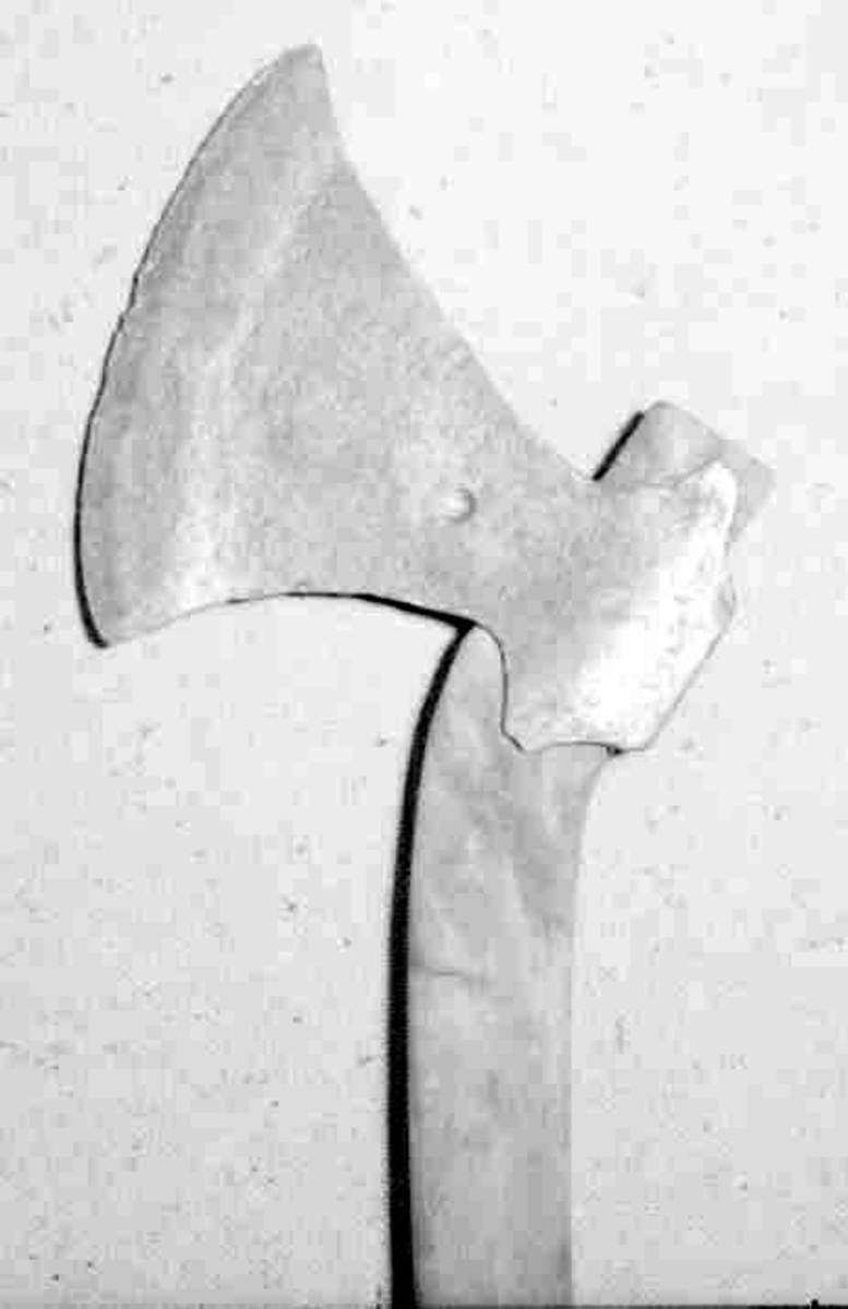 Asymmetrisk blad med lang øvre spiss og kortere nedre spiss. Bladet er tynt og med påsmidd noe tykkere egg.
Øksehammeren har skaftehull og fliker.
Smedmerke formet som et skjell på høyre side.
Nyere uorginalt treskaft.
