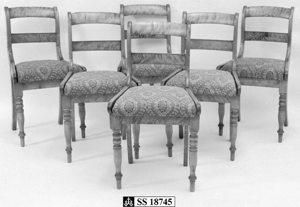 Stolene er i lakkert bjørk i Biedermeier-stil. Stolen har dreide forbein og løst sete med blomstret ulltrekk i grønt, hvitt og svart. Setetrekket er sterkt bleket.