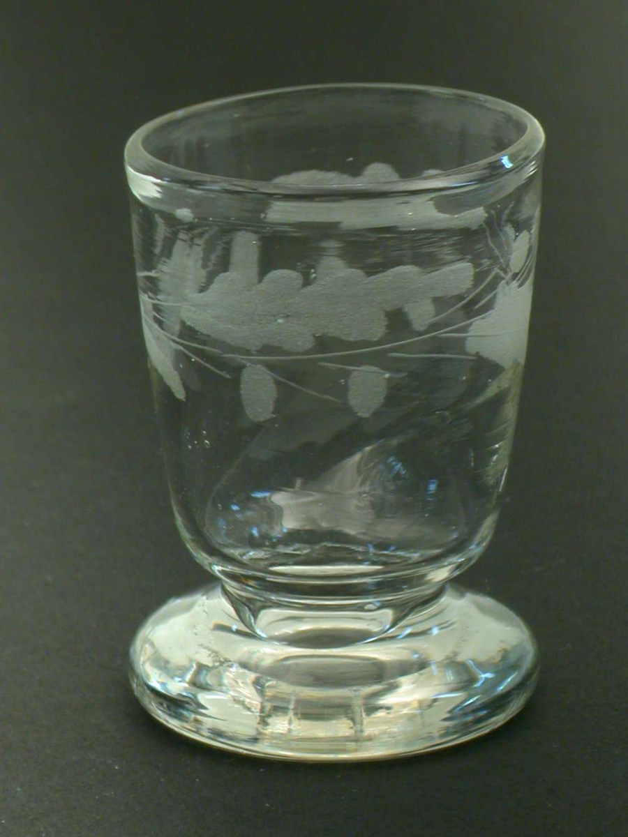 Rundbundet beger med rudimentær stett som nesten direkte forbinder begert med en tykk fot. Glasset har ekeløvsgravyr.