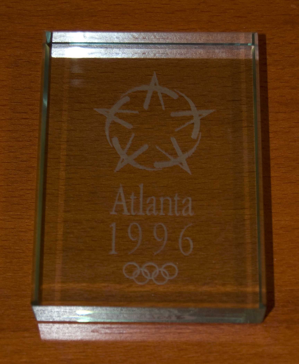 Plakett av glass med motiv av en stilisert stjerne og de olympiske ringene. 