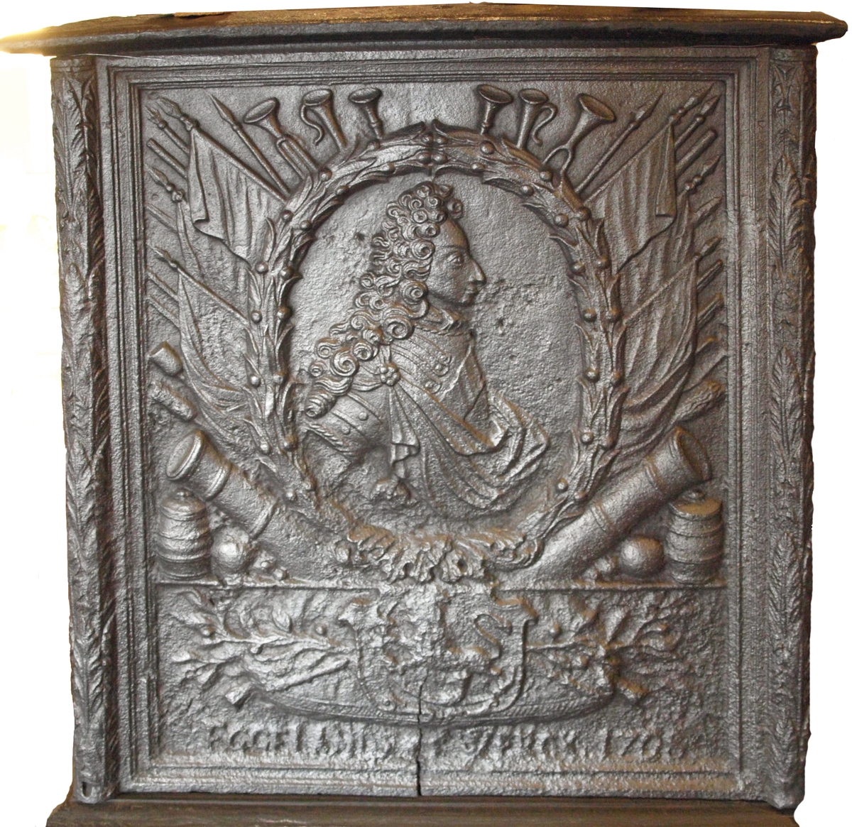 Langsiden med  Frederik 4s brystbilde i profil mot h. i oval laurbærmedaljong, omgitt av krigerske emblemer. Derunder laurbærgrener hvorpå skjold med den norske løve.