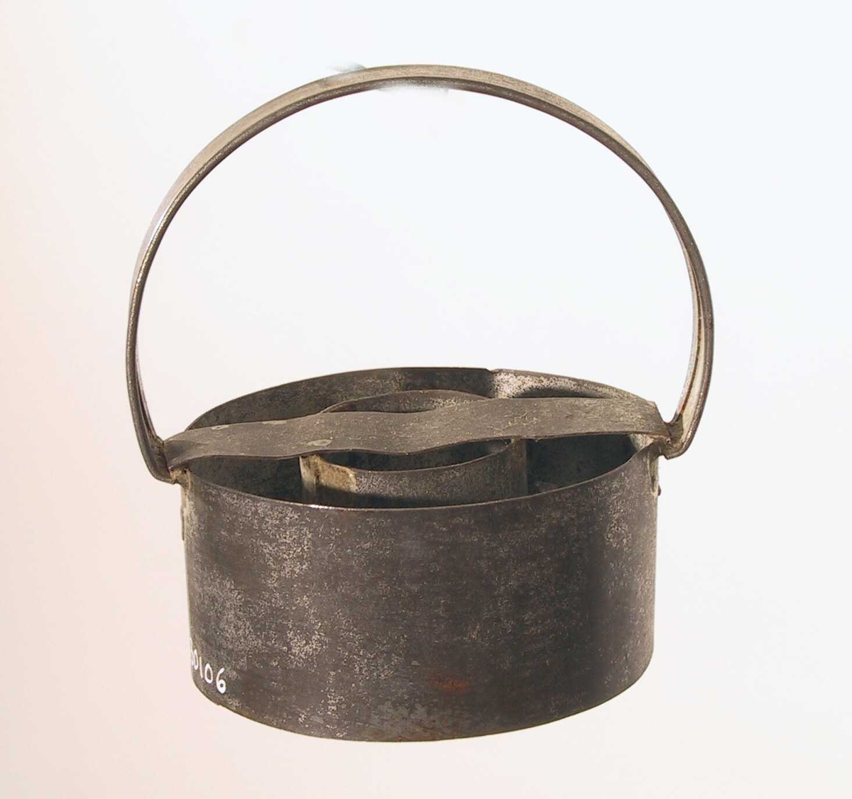 Liten sylinder av tynn jernplate med en større utenfor, festet sammen med et bånd av jern på tvers over begge og et håndtak festet ved hver ende av båndet. 
