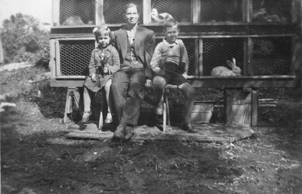 En mann og to barn  foran et kaninbur.