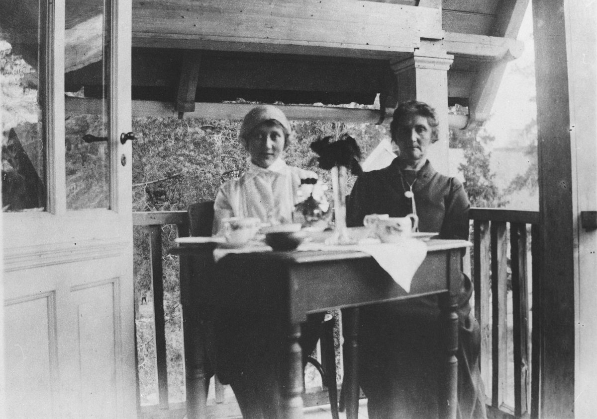 To kvinner sittende ved bord på veranda. Kafeen i Bergersbakken