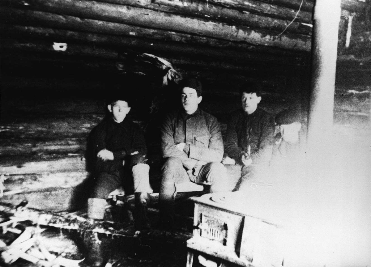 Fire menn ved ovnen inne i koie ved søndre Kyltjern i Losby.