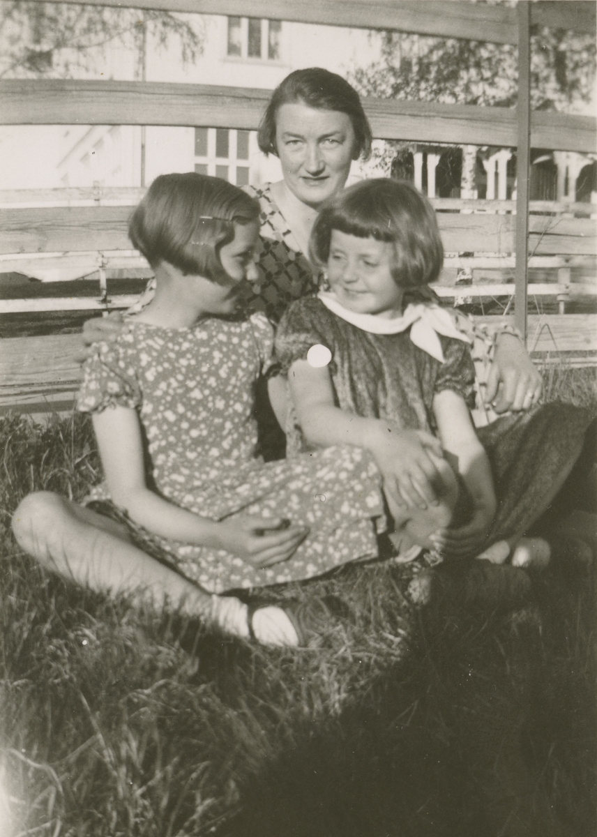 Fru Moe sitter i gresset med de to små jentene Åse Moe og Liv Frogner.