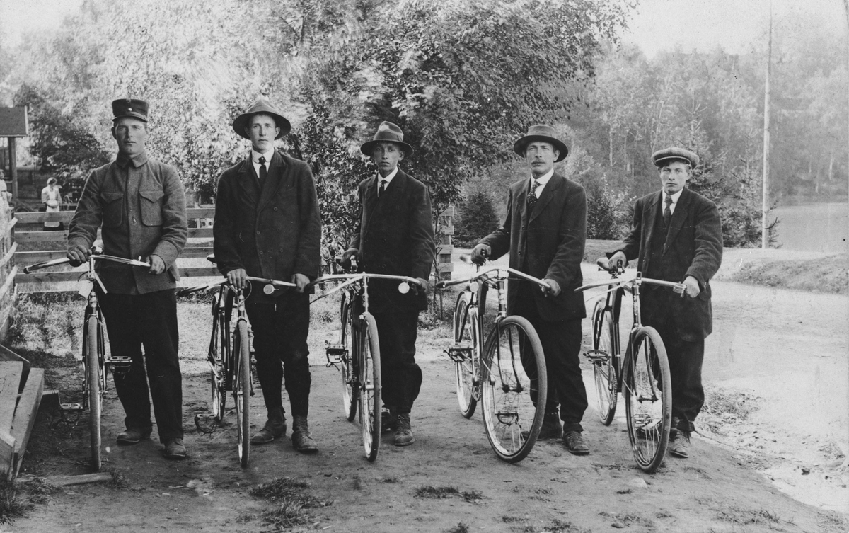 Gruppebilde. Fem menn med sykkel.