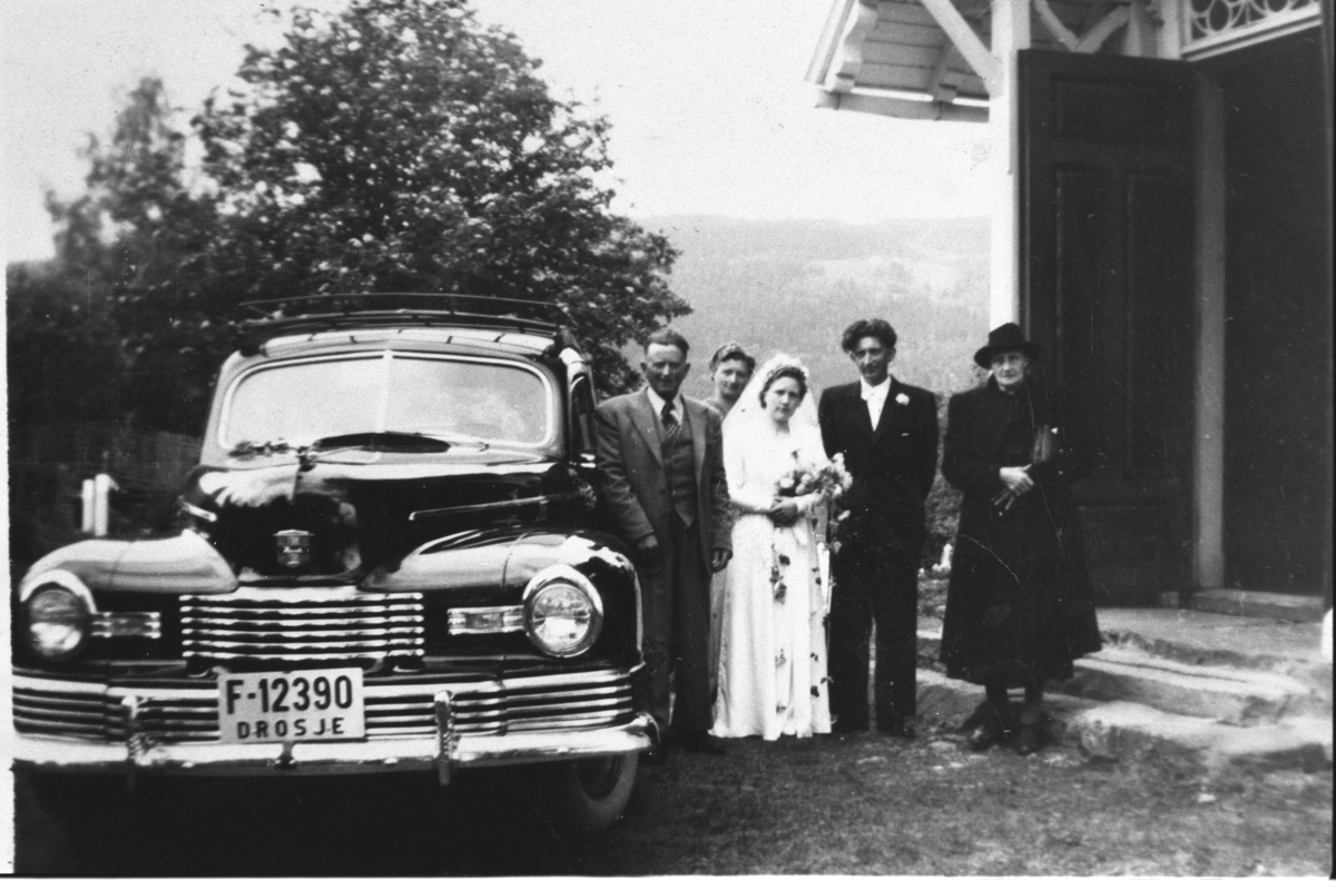 Brudepar utanfor kyrkja, med drosjebilen Nash F-12390 (1946-47 mod)
Framme frå v. Anton Åsarmoen, Kristine Knaldre Åsarmoen, Olav Åsarmoen og Randi Bråten Åsarmoen.