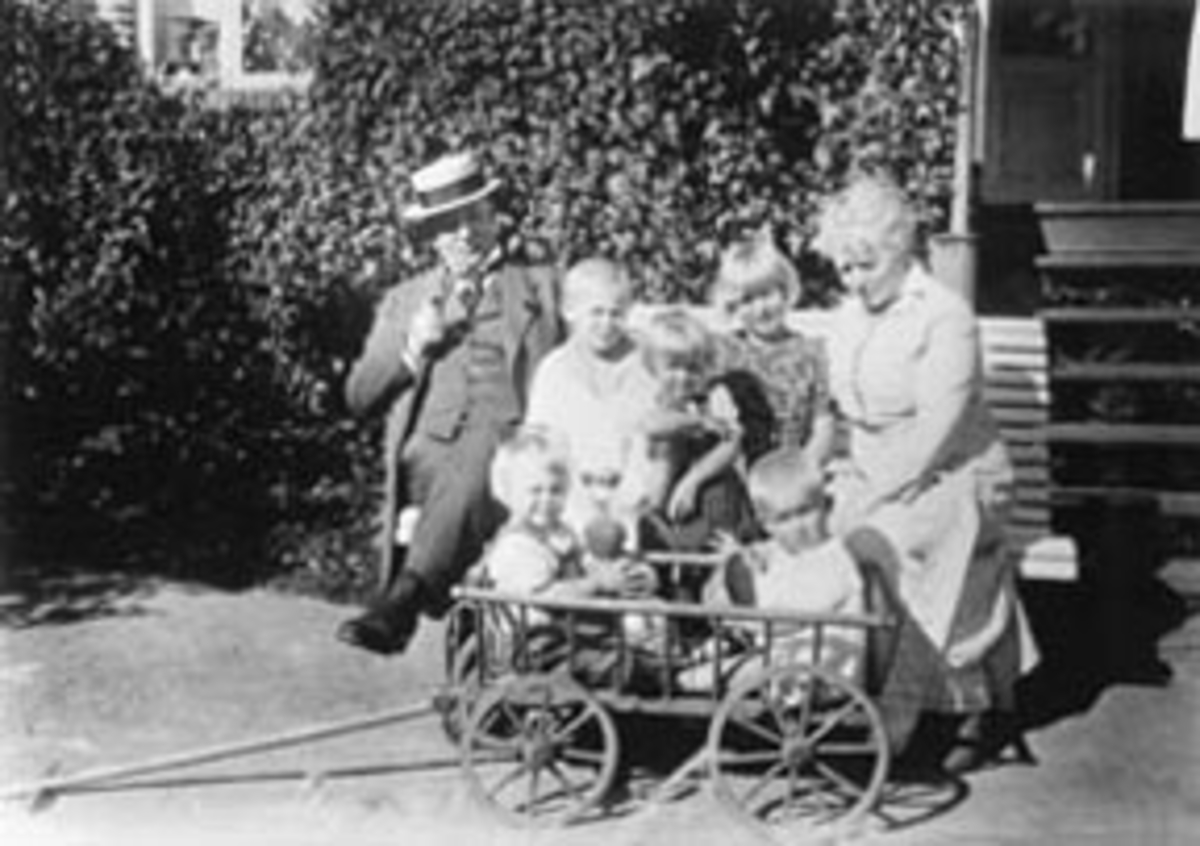 Doktor Karl Løken og Thora Løken med fem barnebarn for huset på Granerud gård, Brumunddal. Lekevogn.