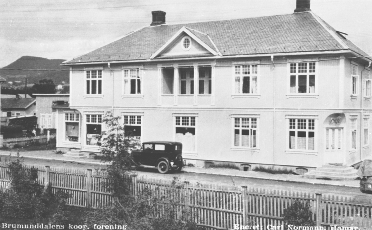 Eksteriør, Brumunddal Kooperative, Samvirkelag, Furnesvegen, kafe til høyre. 
Helgebygården som kooperativen kjøpte i 1917. Bilen er en Ford A-modell 1930-31.