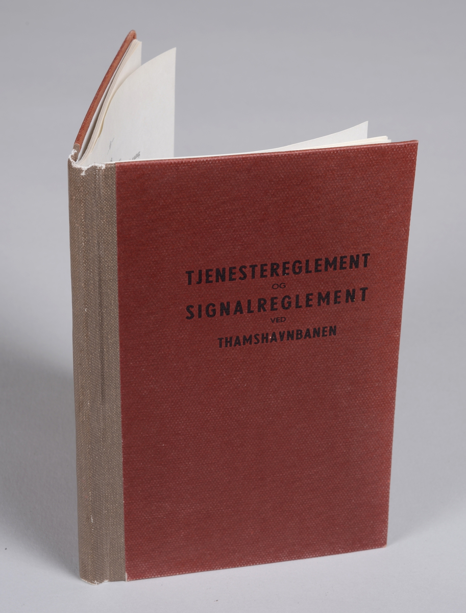 Rektangulær bok med stivt rødt omslag, beige rygg og svart skrift. Omhandler reglement ved Thamshavnbanen.