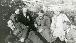 6 personer sitter ute på en gressbakke, fiskehjeller i bakgr