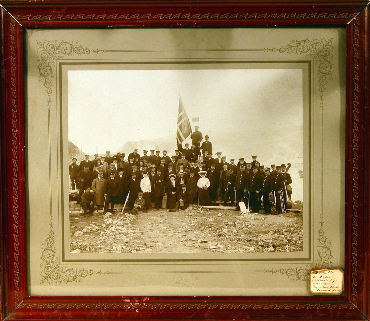 Gruppebilde tatt av deltakere på D/S "Kong Harald"'s turisttur Spitsbergen - Hollandsbugten 1906. Bildet antagelig tatt på Danskeøya v/  Andréestøtten, Andrée-ekspedisjonens base.
