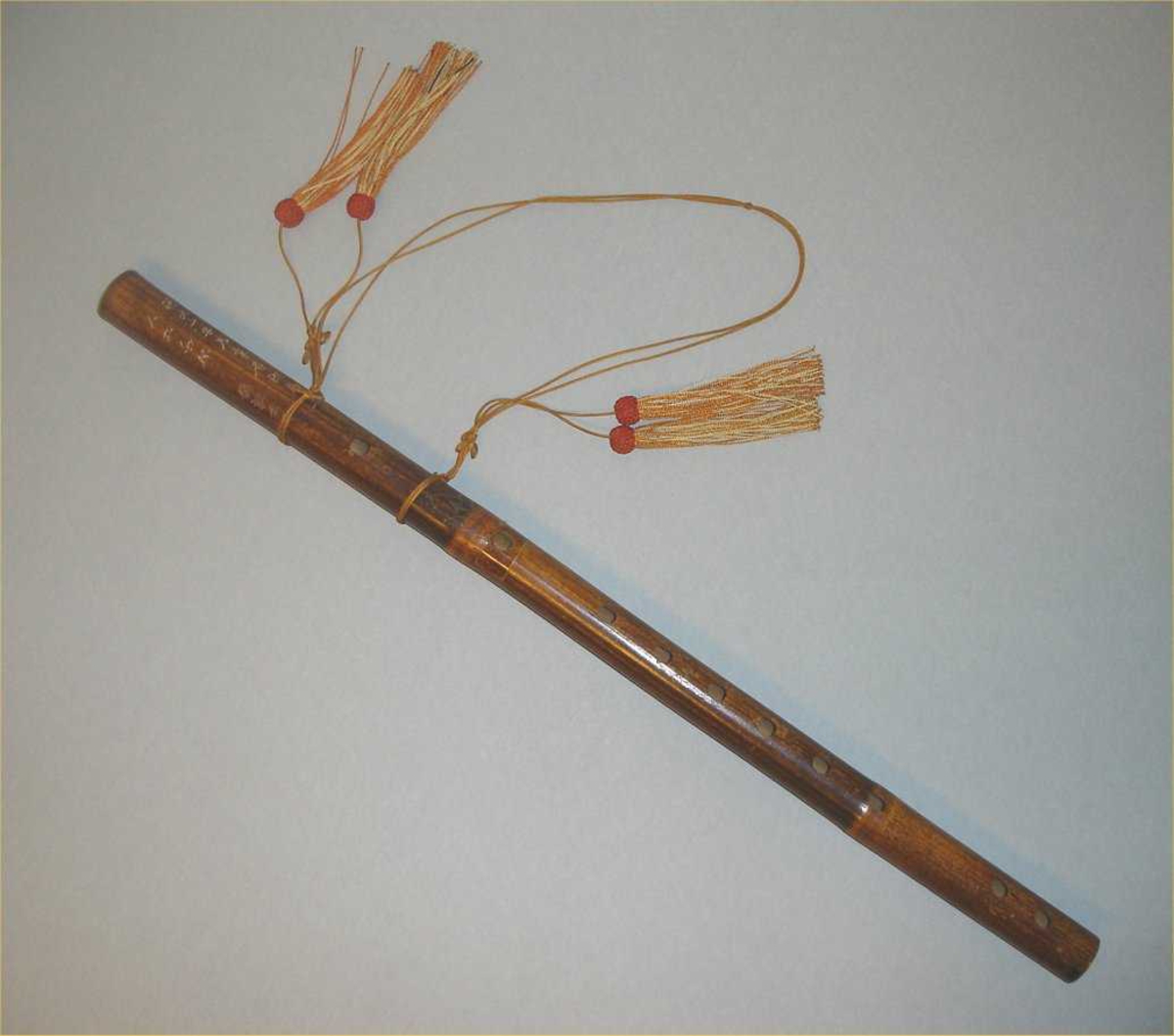Tverrfløyte av et stykke lakkert bambus. 12 hull: 6 fingerhull, 4 stemmehull ved nedre ende, og mellom blåse-og fingerhull et hull dekket av et membran.
Fløyten dekorert med kinesiske skrifttegn. En lang silkesnor med fire silkedusker er festet til fløyten.