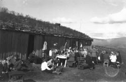 Stor seterstue med mange folk utenfor som drikker kaffe.