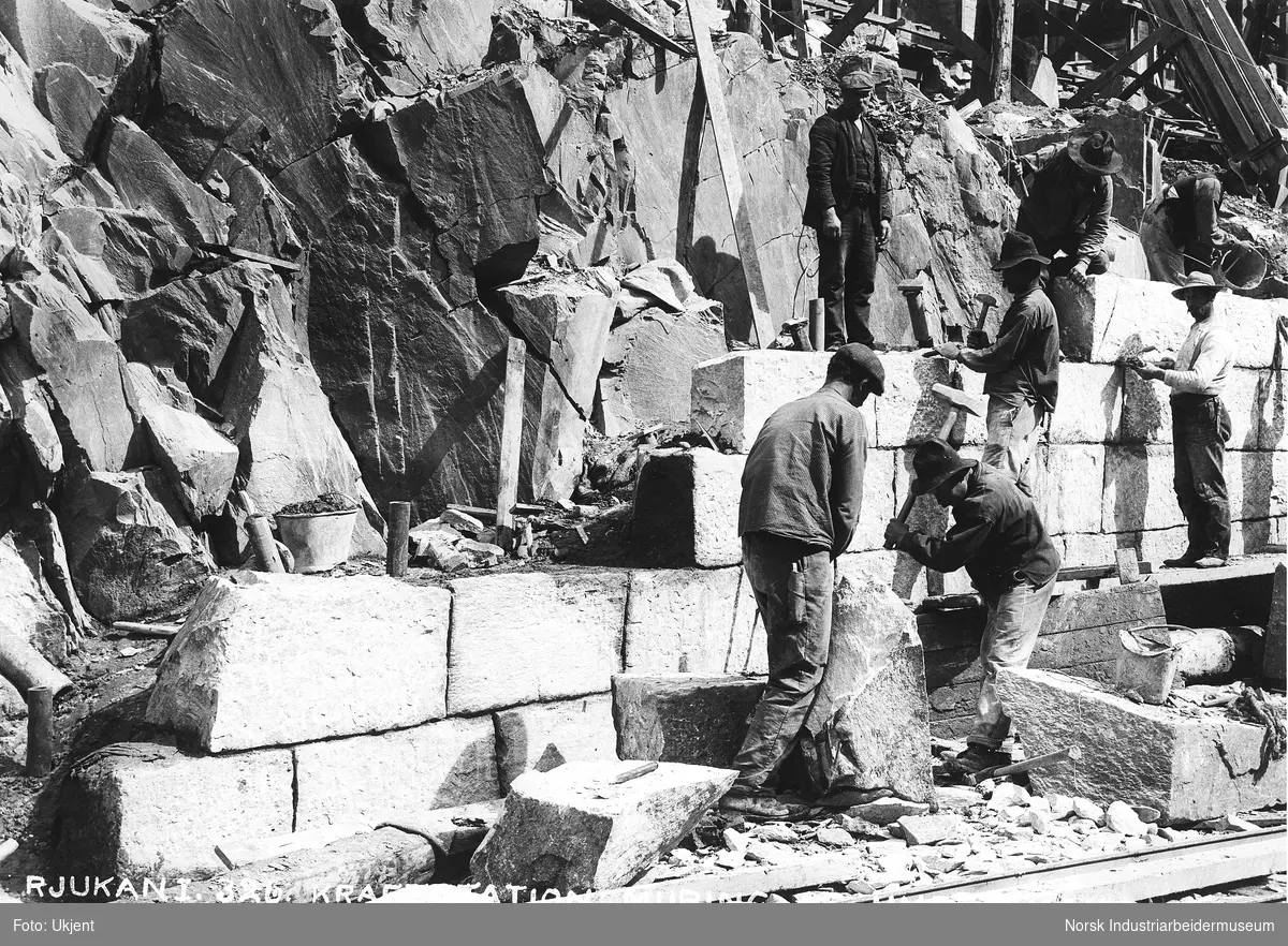 Rallare i arbeid med å mure undervannskanalens vegger på Vemork. Steinblokker legges på plass og meisles til.